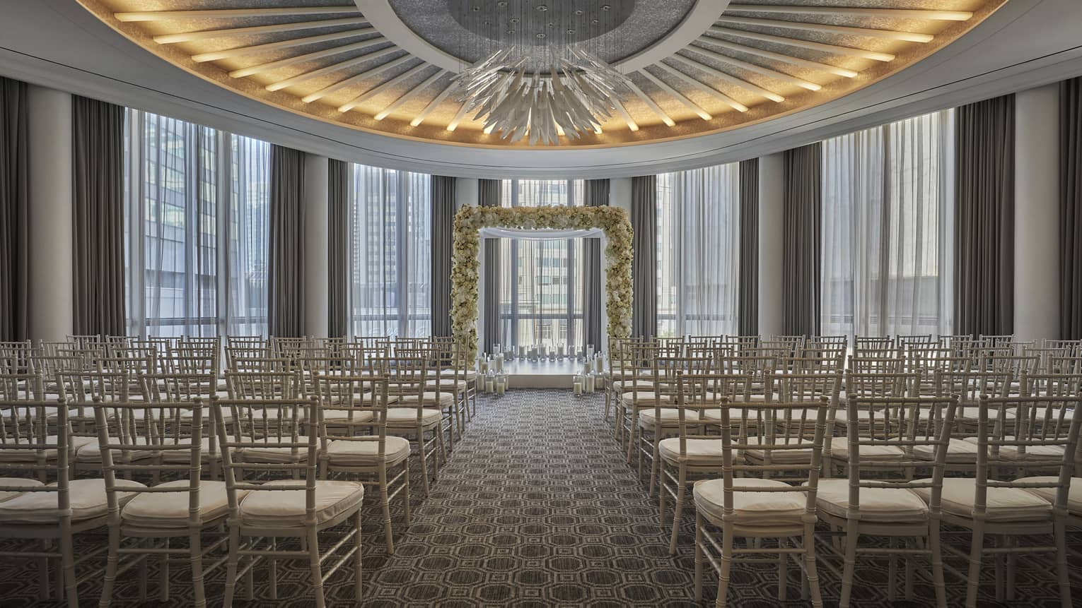 Four Seasons Boston One Dalton Ballroom is ready for a ceremony with rows of white rattan chairs and a white floral arbor