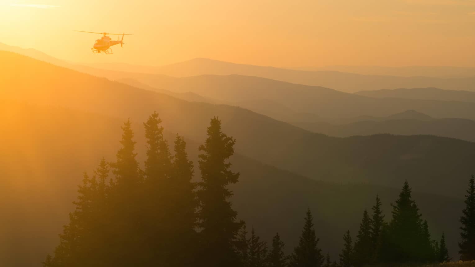 Helicopter at sunset flying over Aspen Mountain in the Elks Mountain range
