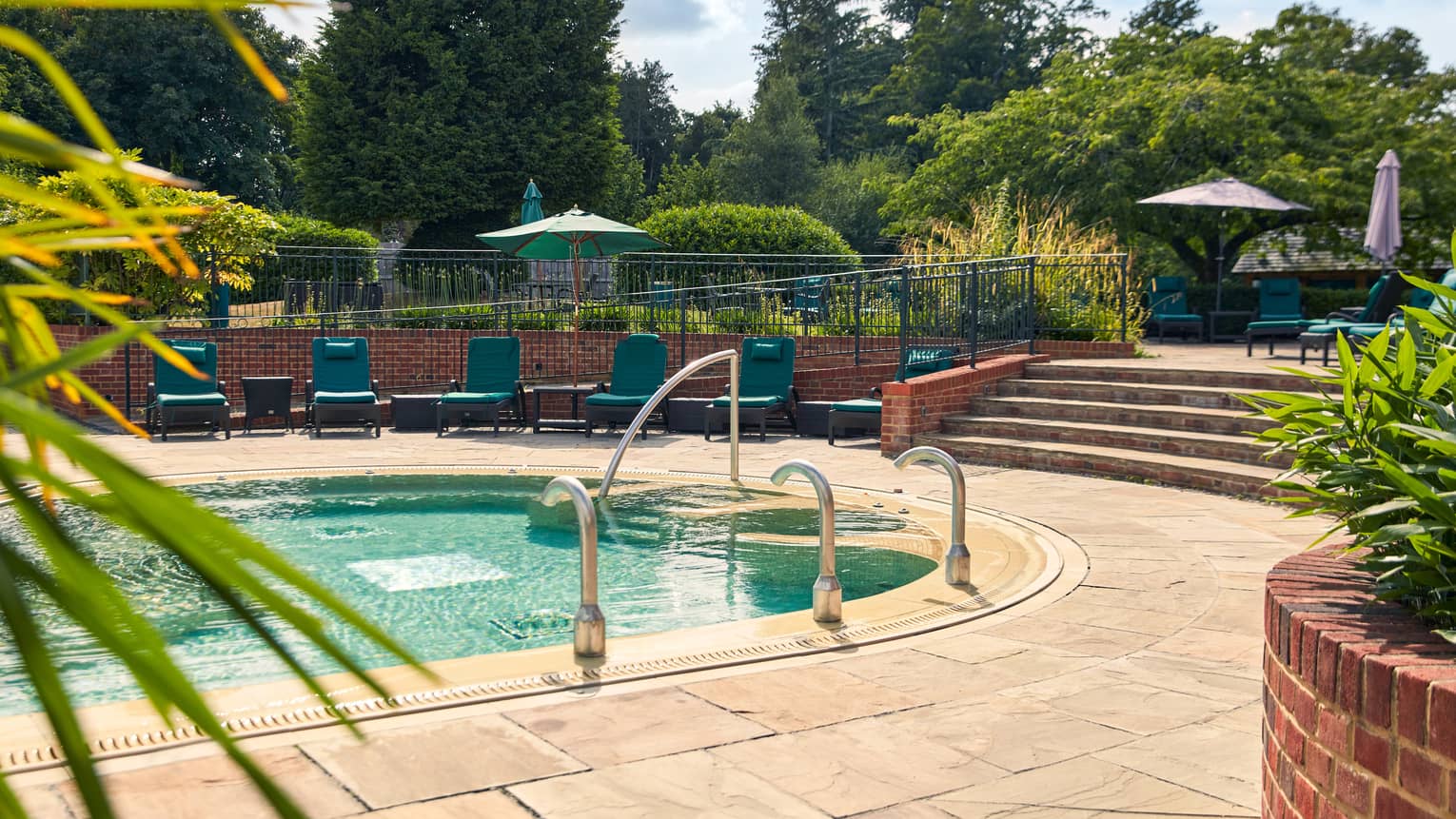 Outdoor pool with flagstone surround, green lounge chairs and stairs leading up to area with umbrellas