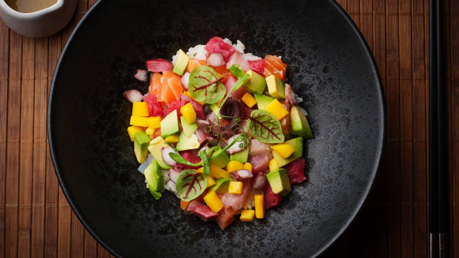 Raw seafood and vegetables with rice in a black bowl.