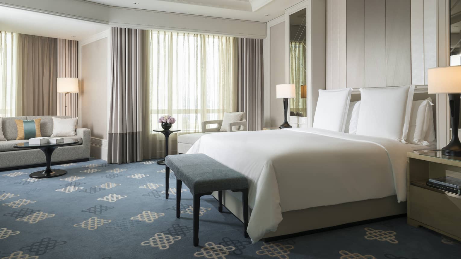 Spacious hotel room with blue pattern carpet, king sized bed and white bedding