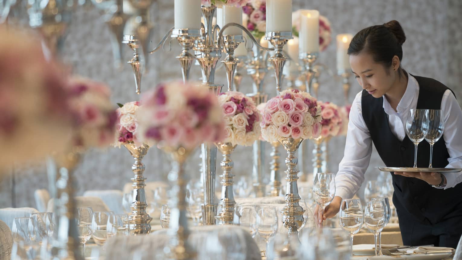Hotel staff sets wine glasses on Peony Ballroom banquet table with pink flowers, tall candles