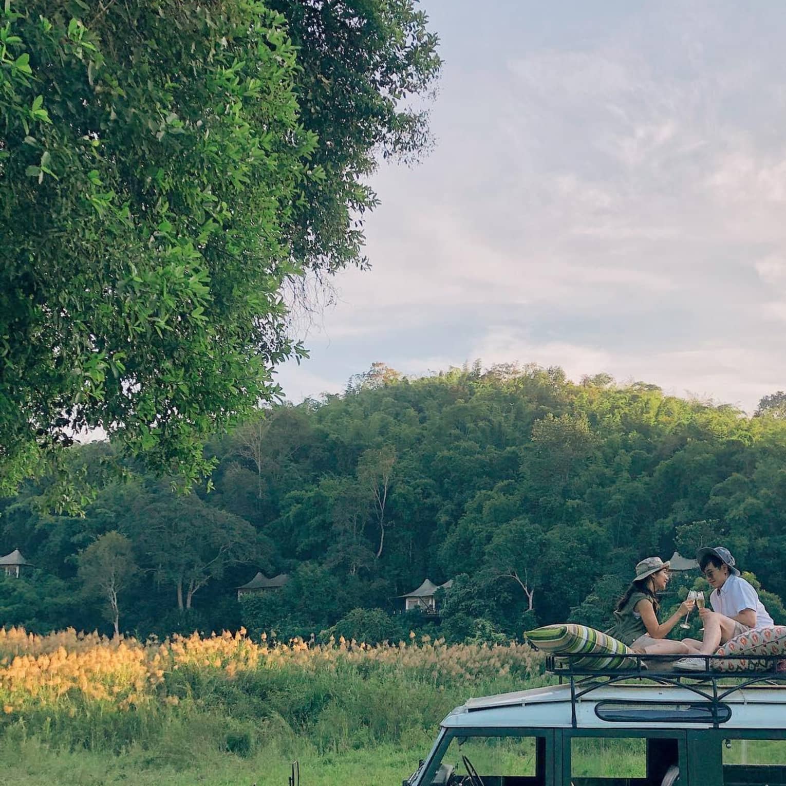 Two guests sit on top of a safari vehicle in a field