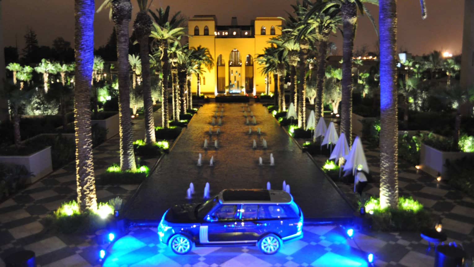 View over Solano Terrace at night, blue lights over Range Rover parked by long fountain between palms