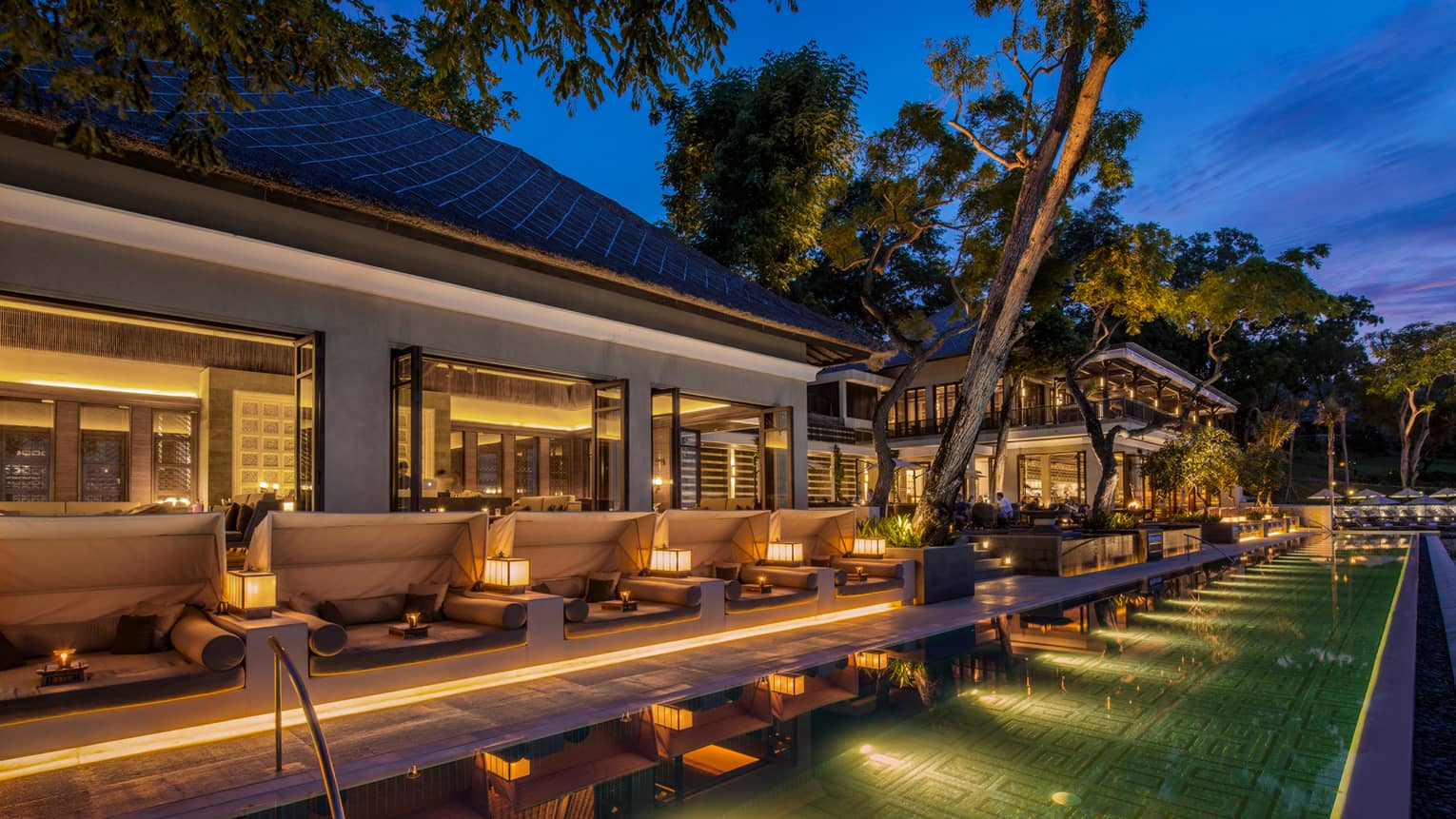  Sundara illuminated swimming pool at night lined with white patio sofas, candles 