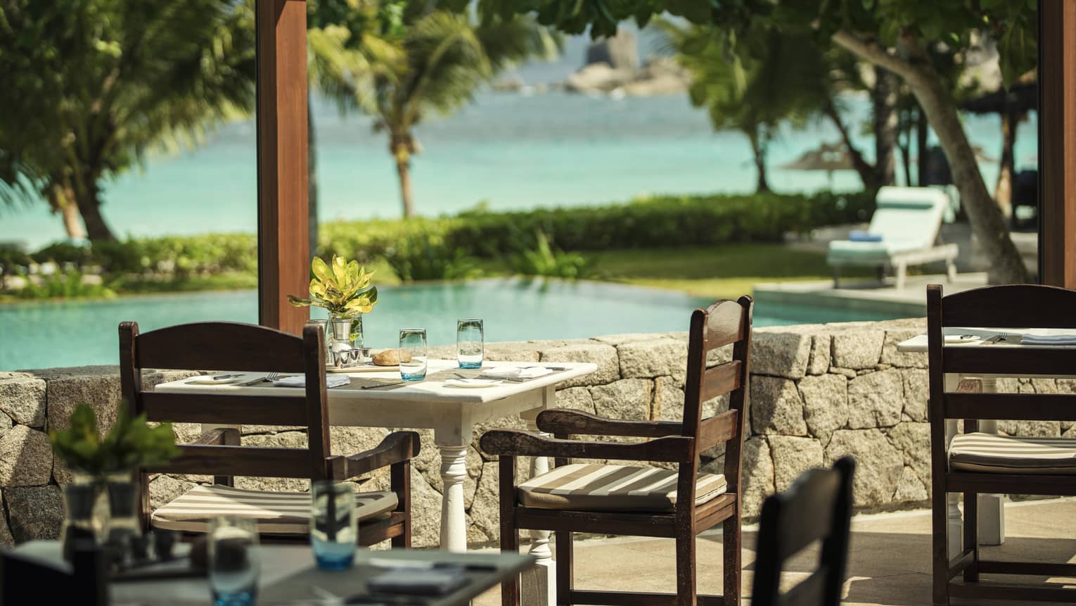 Outdoor dining table and chairs overlooking pool with tropical foliage