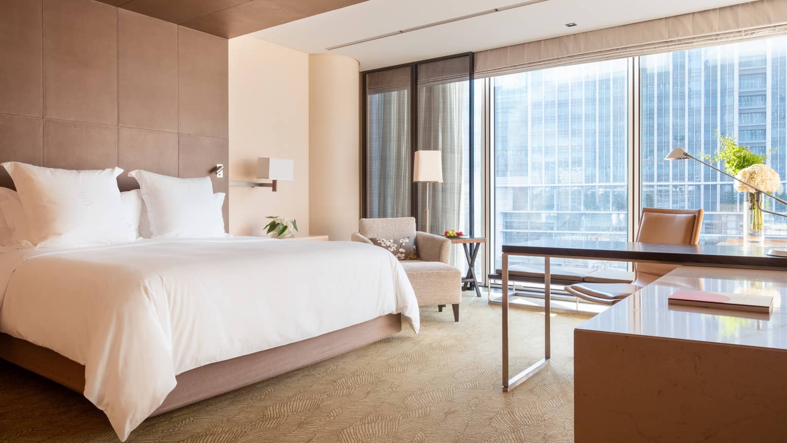 Guest room with large windows, city views, king bed, lamp, armchair and workspace