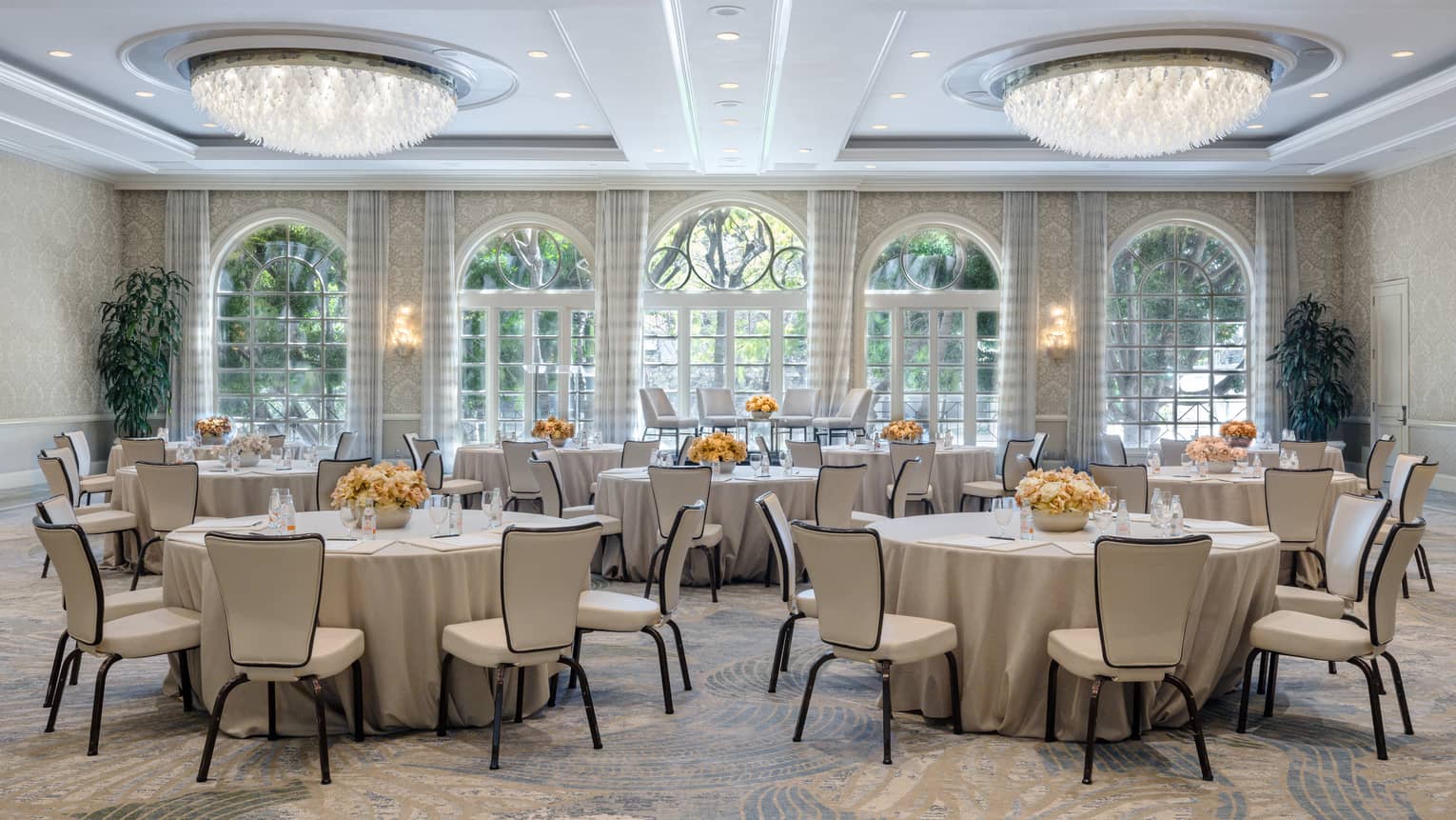 Ballroom with five round banquet tables, dual chandeliers, beige patterned carpeting and floor-to-ceiling windows