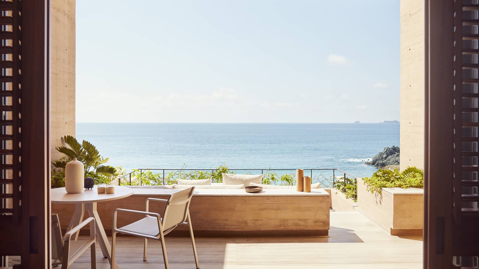 The exterior of a beachfront room with a small table and a large opening looking out at an ocean.
