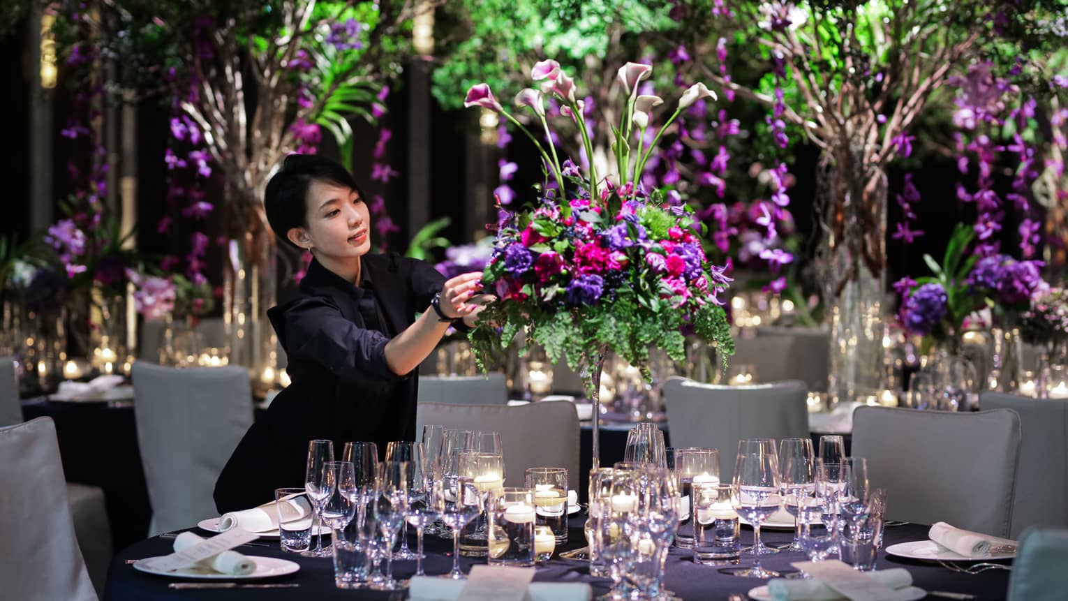 Wedding event staff arranges large floral centrepiece on banquet table