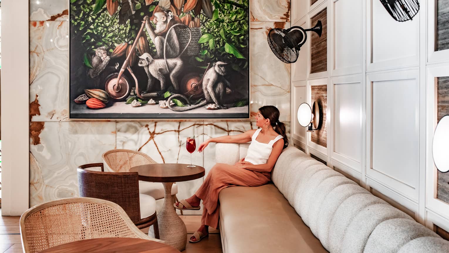 A woman sitting at a booth near a painting of monkeys.