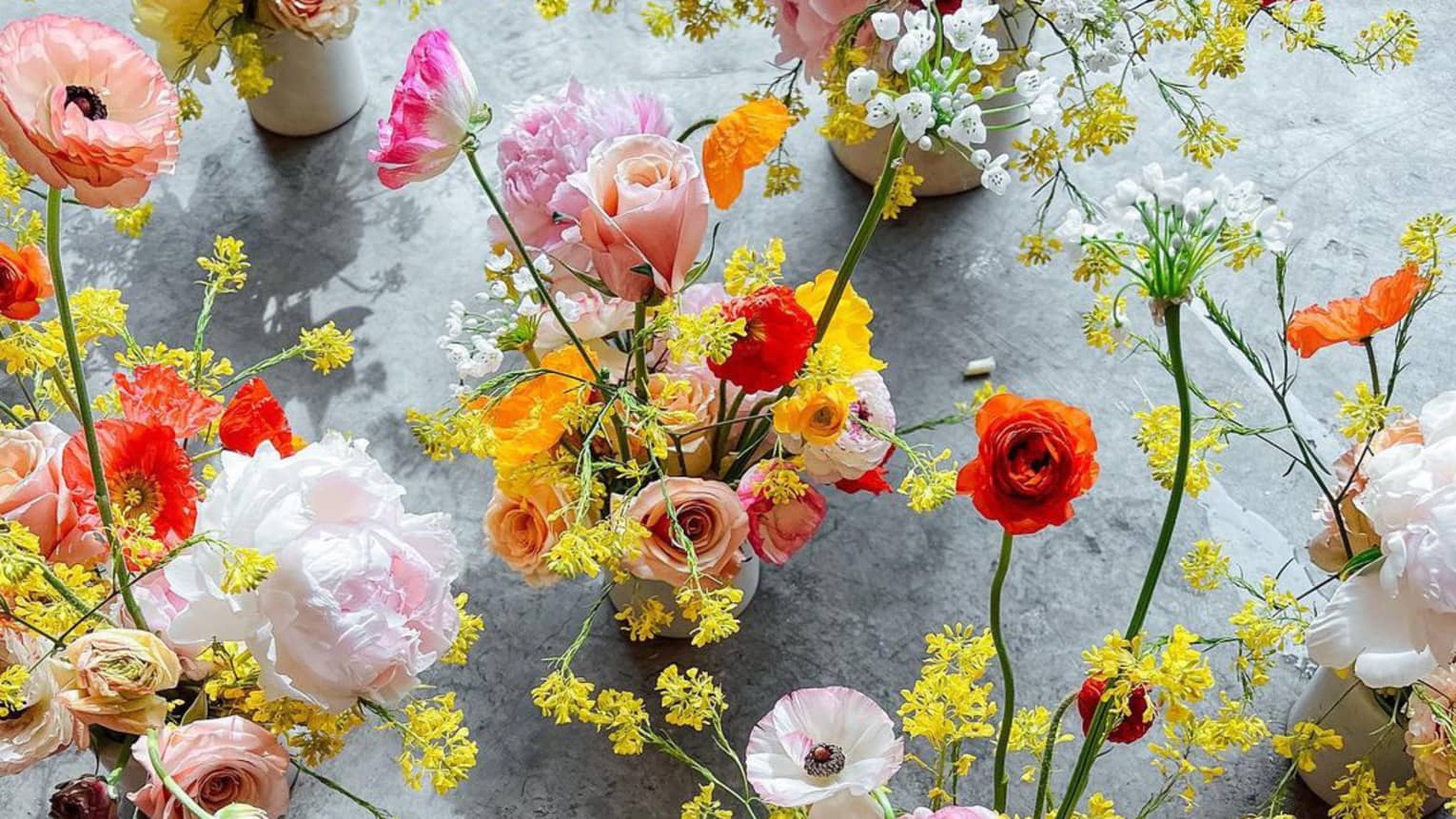 A variety of flowers in vases on a grey ground.