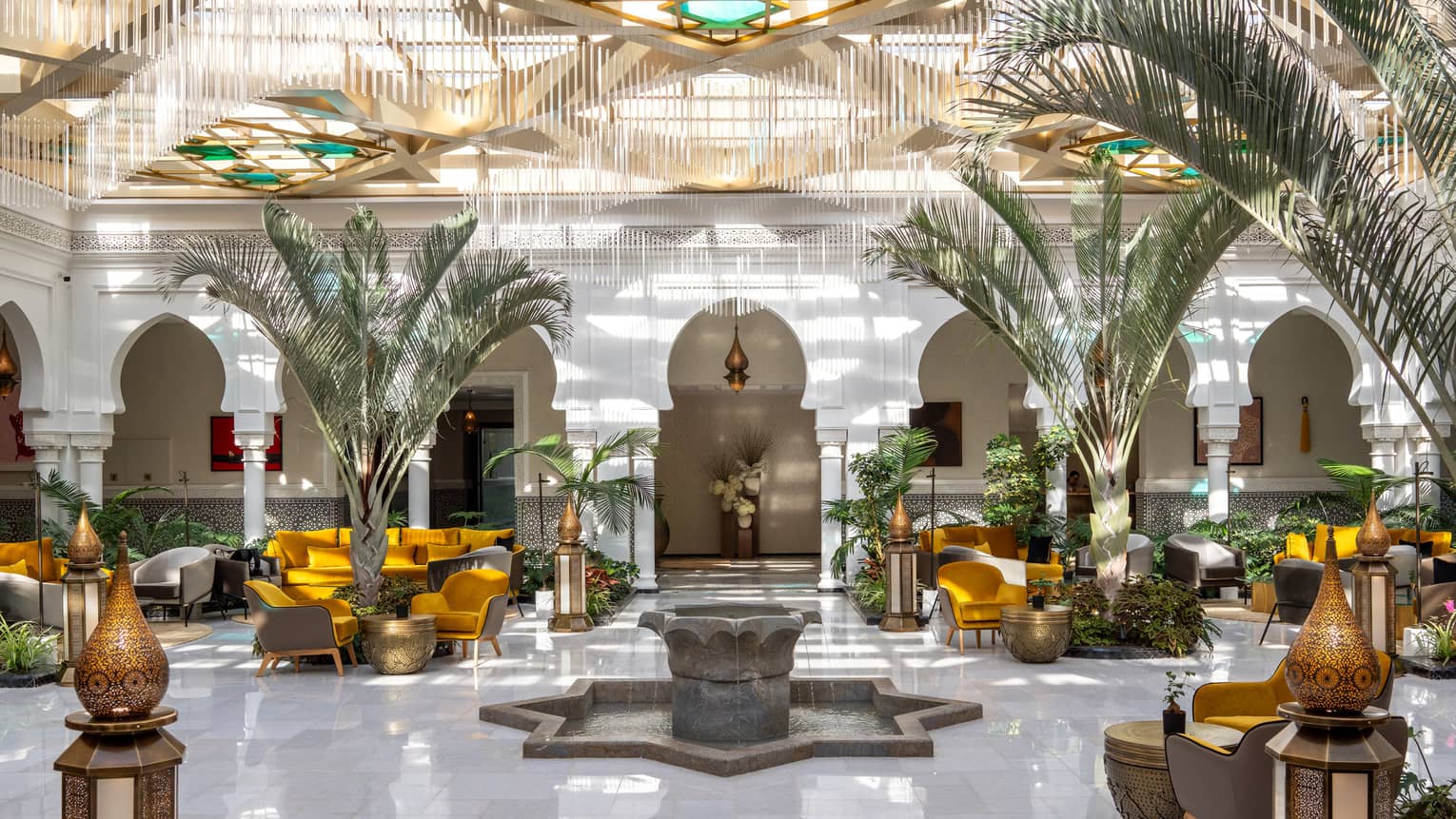 A light-filled atrium of luxury hotel featuring a palm trees and lobby lounge with yellow chairs