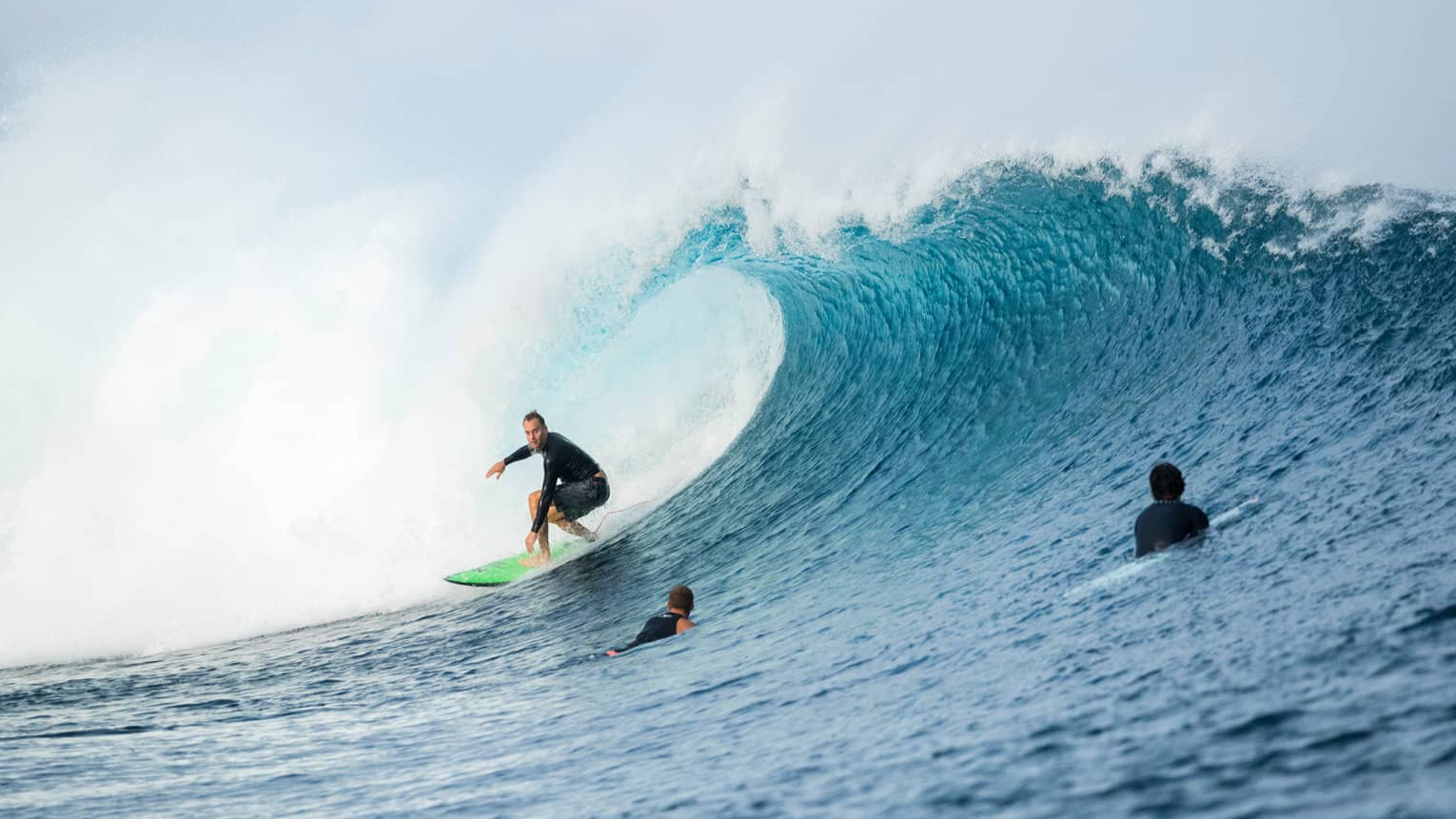 Surfer rides surfboard on large wave, two surfers swimming in water