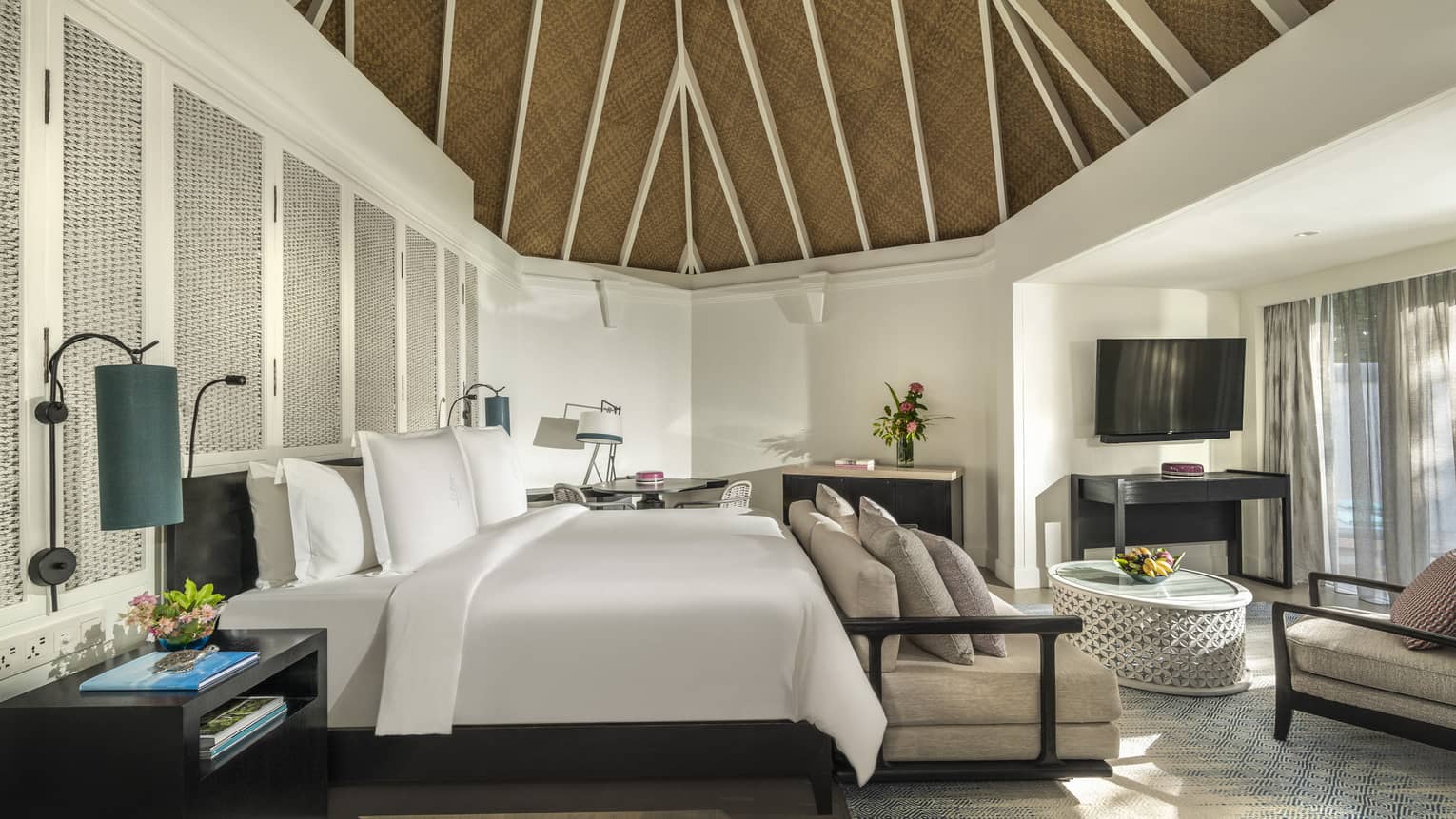 Beach pavilion bedroom with a king-size bed, vaulted thatched ceiling, cozy seating area and a flatscreen TV