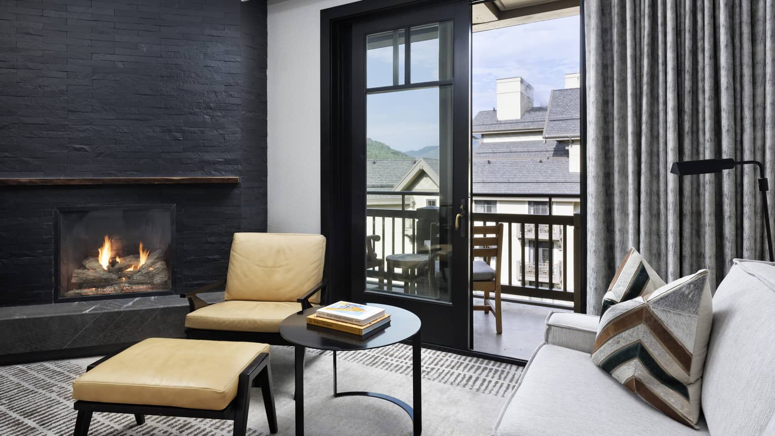 White sofa, corner stone fireplace, arm chair and ottoman, sliding glass door leading to balcony