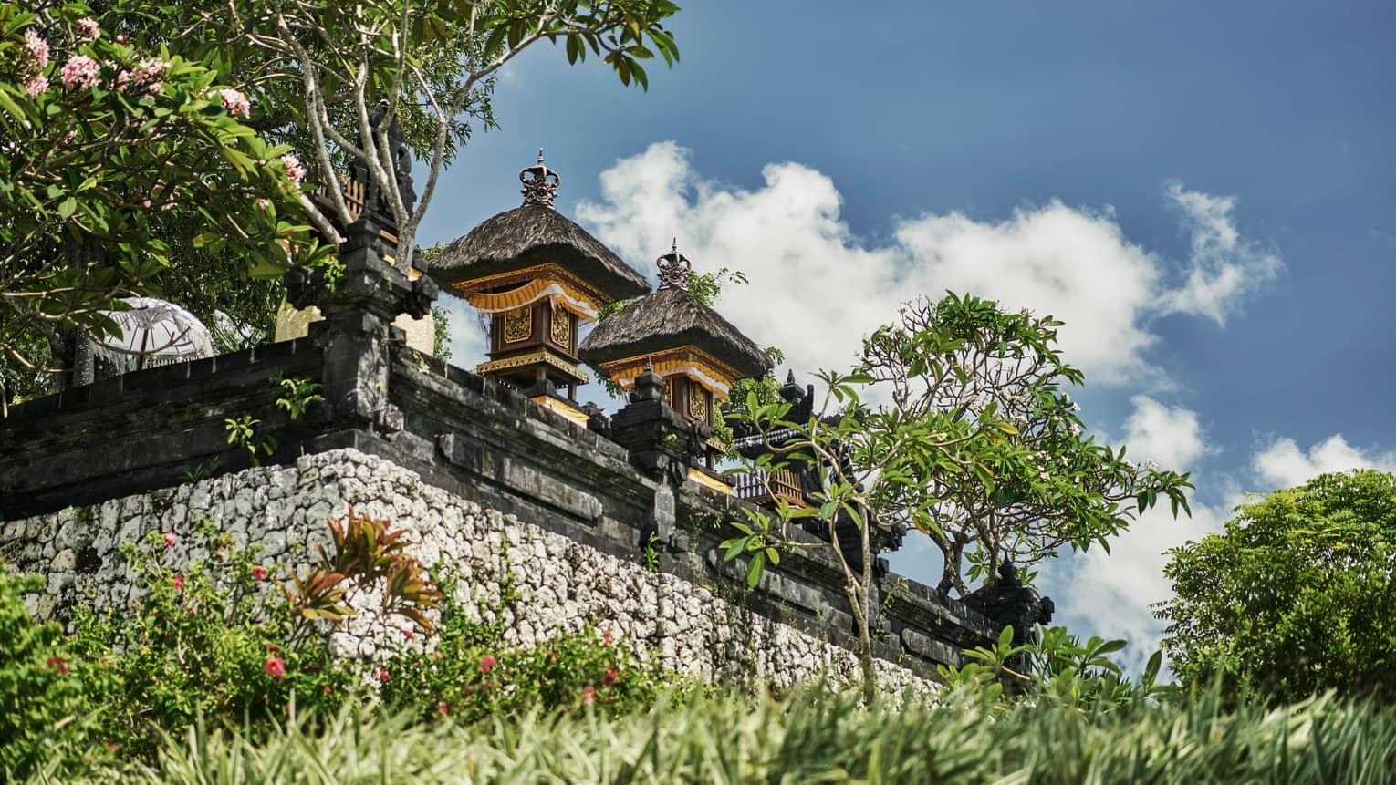 Exterior view of resort temple with stone wall, posts and carvings, tropical trees