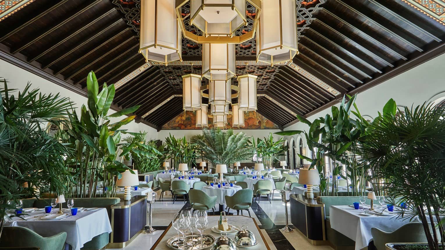 Historic Peacock Alley restored dining room with high ceilings, art deco-style chandeliers and tropical plants
