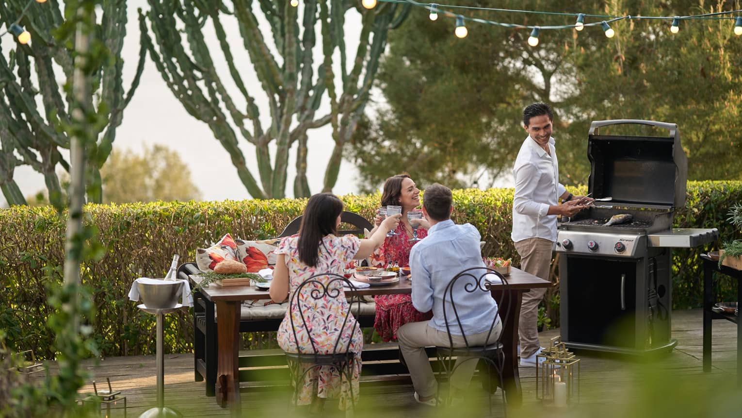 A group of four people grilling food outside at a large table while wearing nice beach clothes.