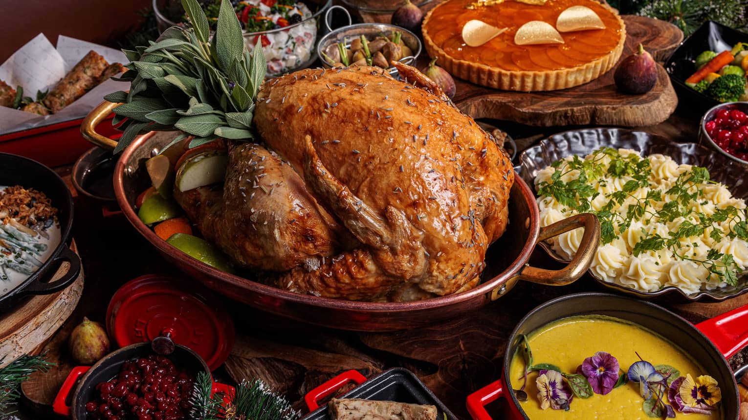  A whole roasted turkey, a platter of mashed potatoes, a bowl of yellow soup, an orange-colored tart and a small bowl of cranberry sauce fill a holiday table