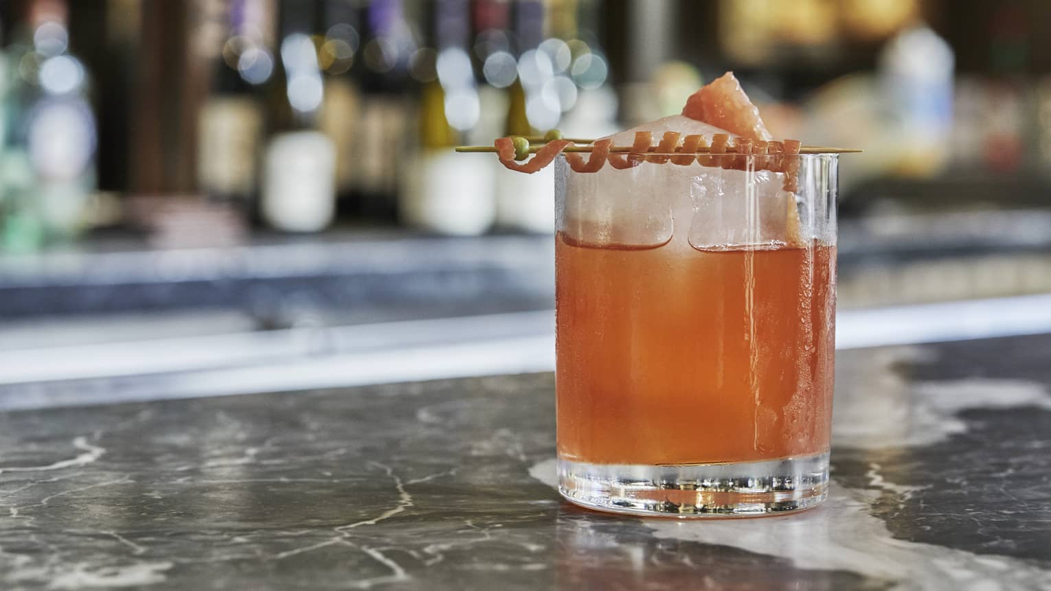 A cocktail with geometric ice and a decorative curled rind on a marble countertop 