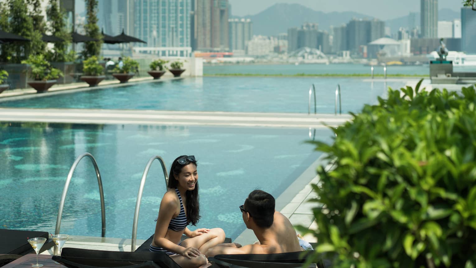 Couple wearing swimsuits on outdoor swimming pool deck, city skyline in background