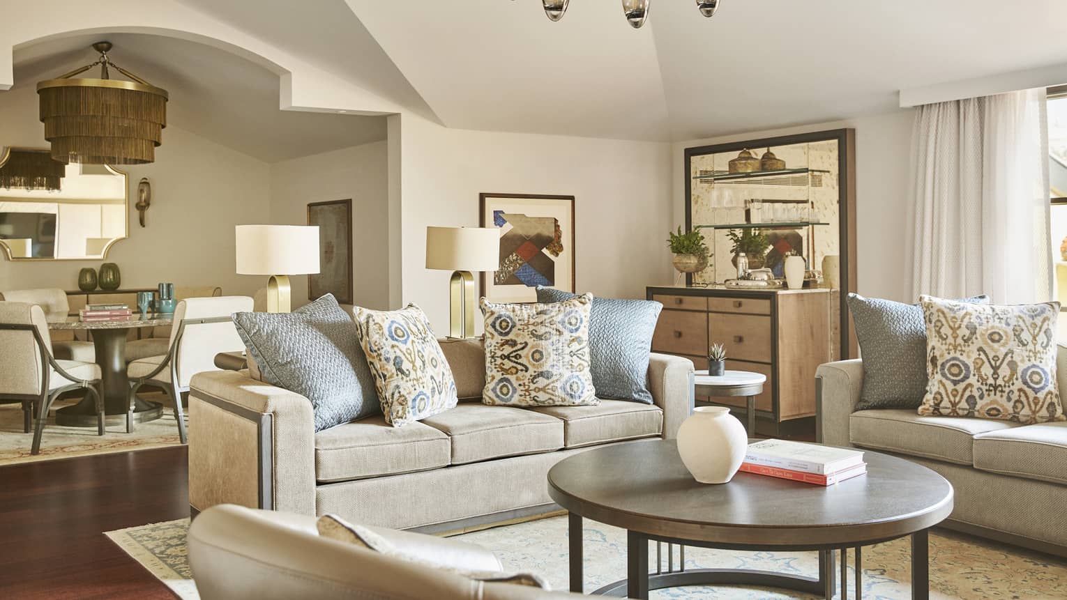 Hotel suite grey living area with round coffee table and neutral dining area in back