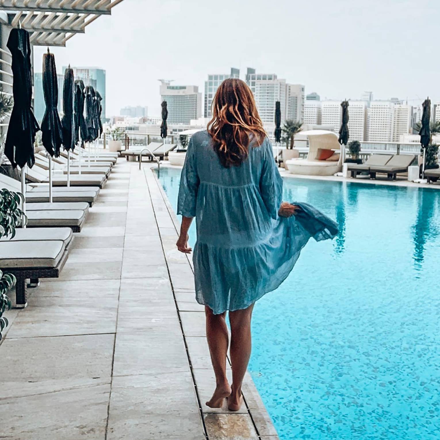Back of woman walking across outdoor swimming pool deck