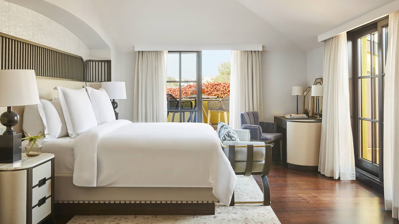 White Four Seasons bed flanked by nightstands and lamps, and tall windows with long white curtains on two walls