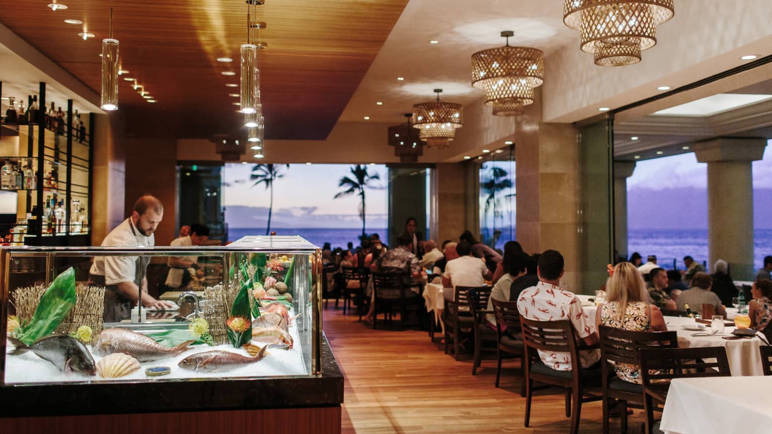 Chef prepares seafood at a sushi bar in a beachfront restaurant during sunset