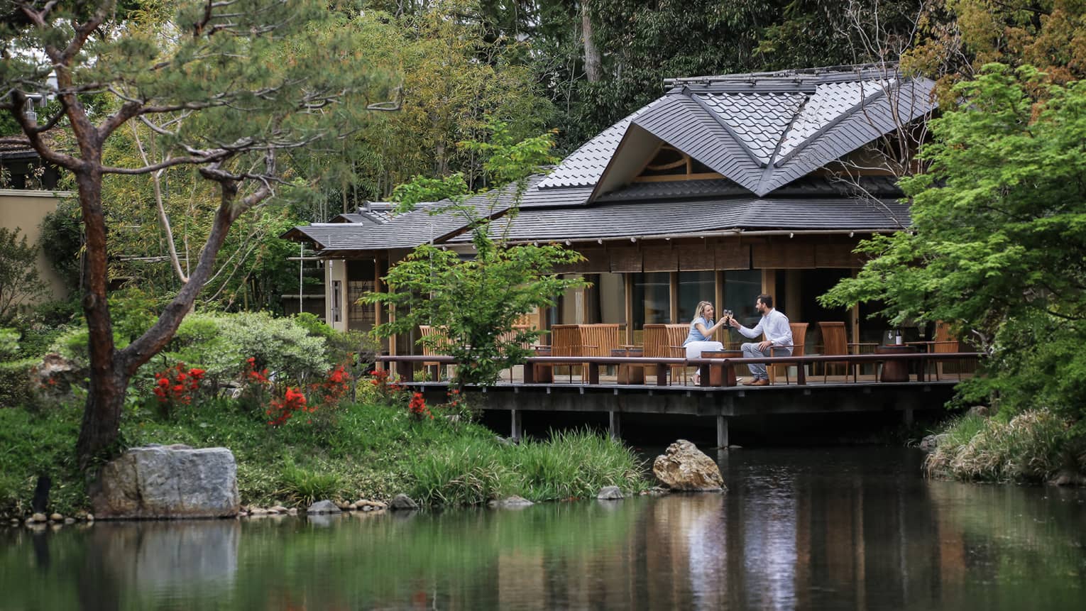 View across pond to restaurant patio where couple toasts with wine glasses