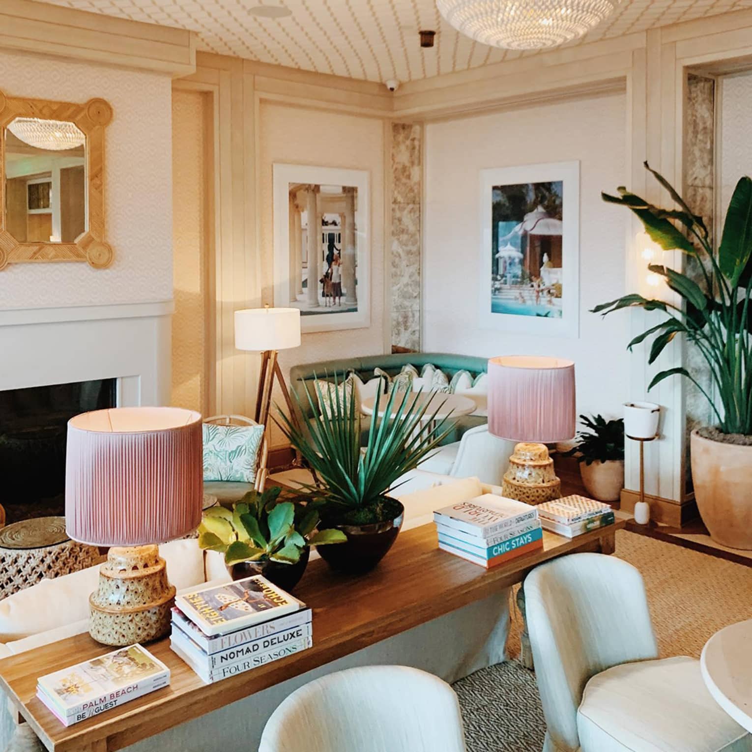 Elegant dining room with pink and white accents, palm plants, and travel books on the console table, creating a sophisticated and inviting atmosphere.