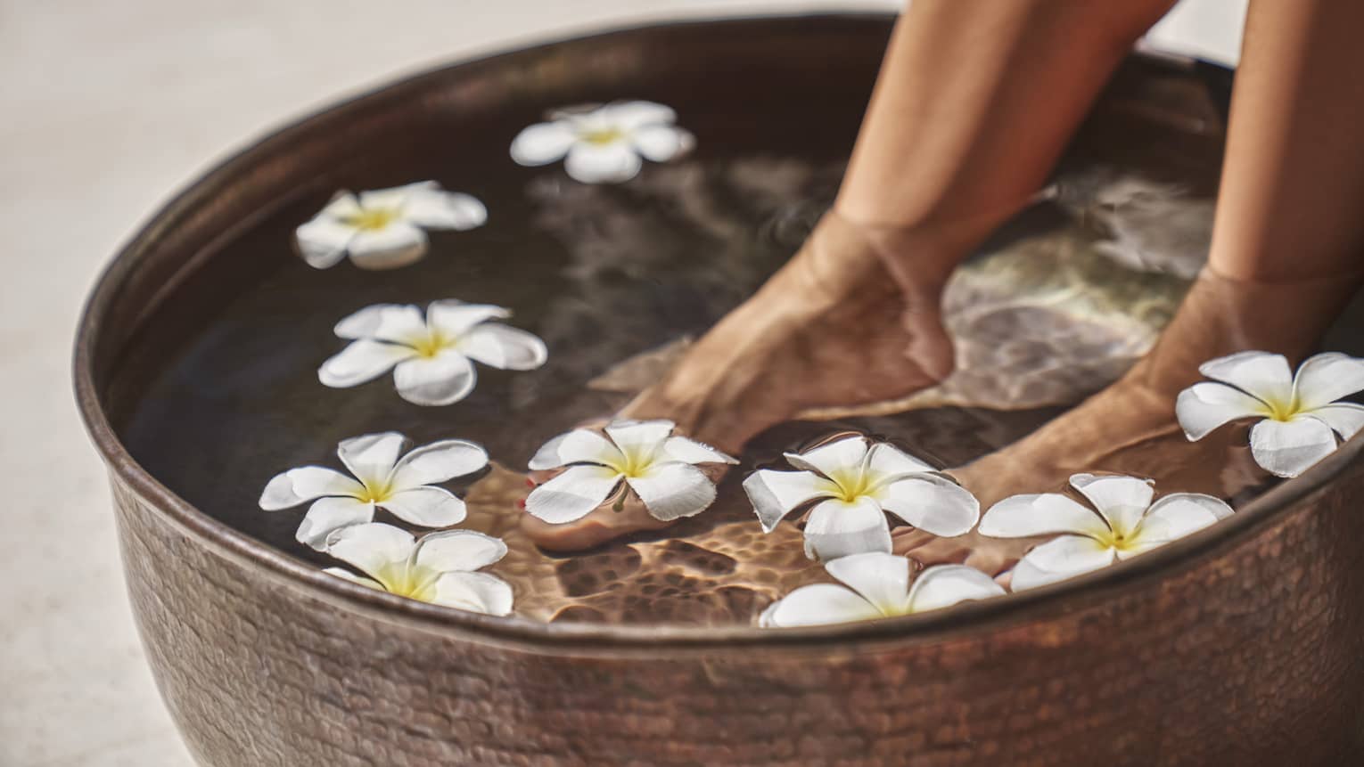 A woman's feet in a bowl of water and flowers.