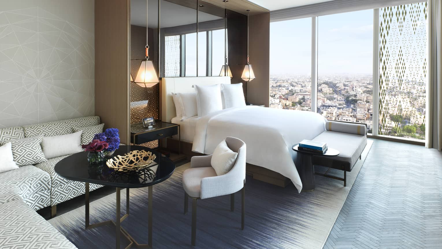 Ambassador Suite L-shaped sofa, table and chair beside bed, floor-to-ceiling window