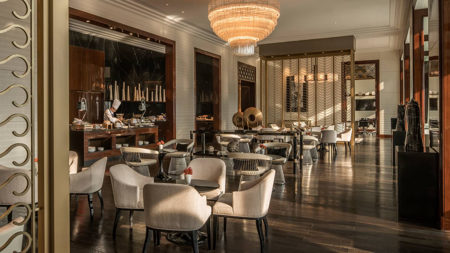 Executive Club lounge chef at bar by cocktail tables, chairs under tiered crystal chandelier