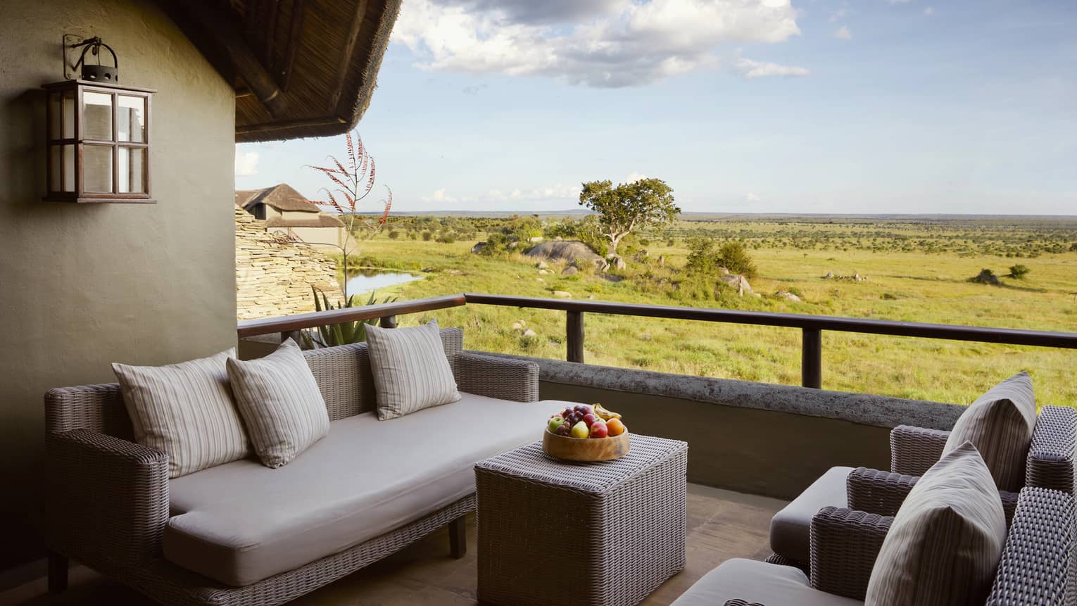 Villa terrace with beige wicker sofa and two chairs and expansive plains under blue skies