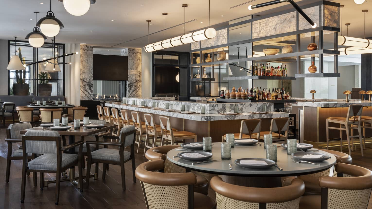 The interior of a well lit restaurant with wood and grey accents and a large bar area.