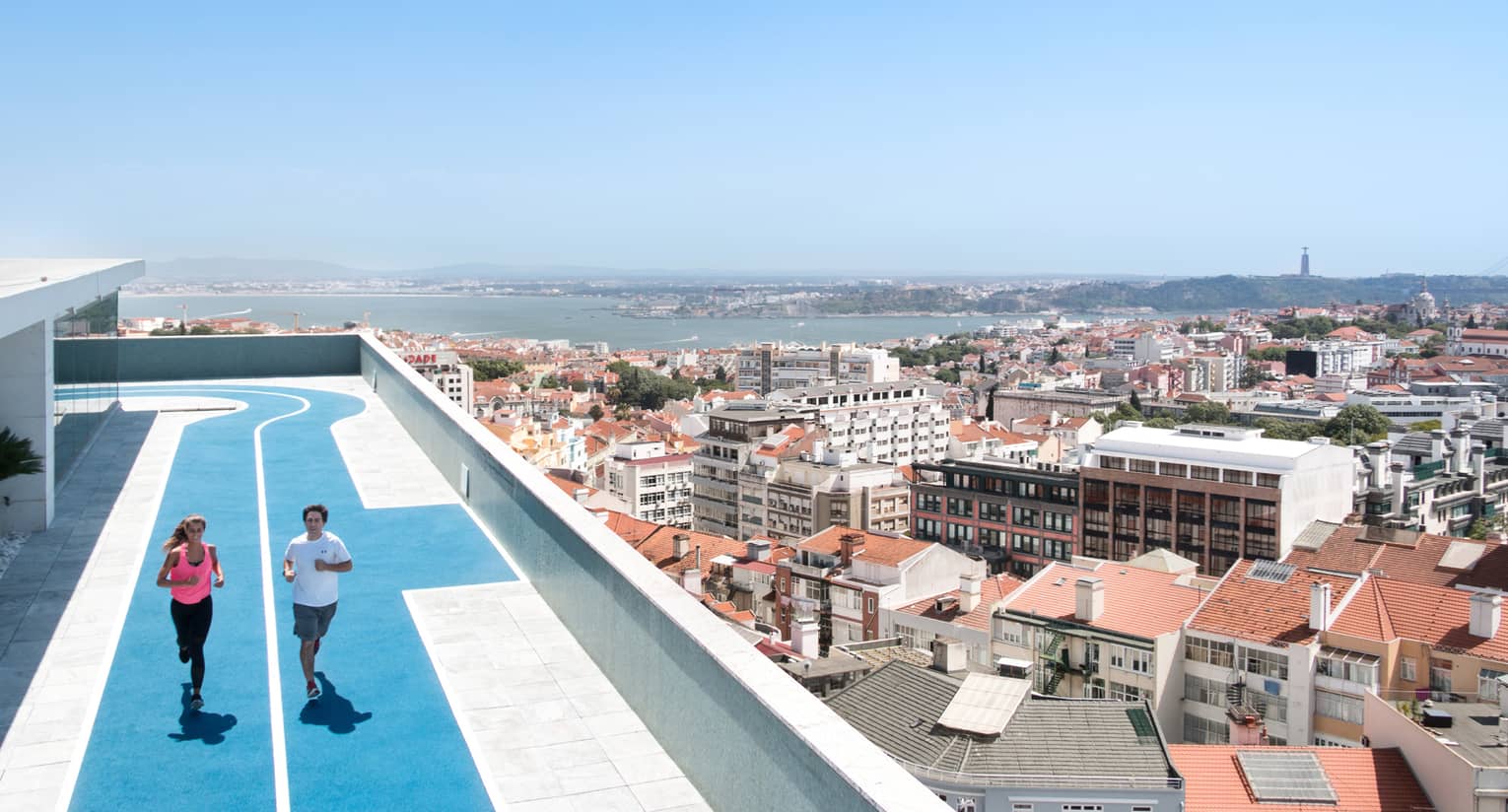 Two people run on blue, rooftop running track, overlooking Lisbon