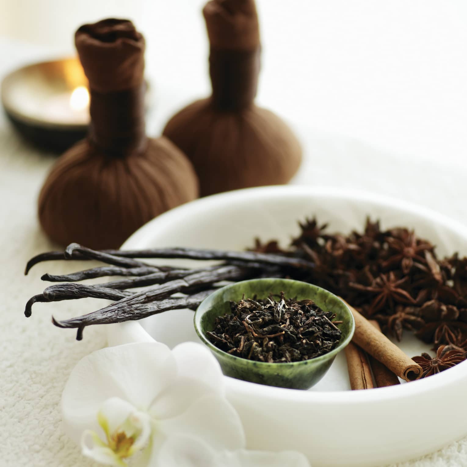 A white bowl filled with various spa ingredients like vanilla bean, star anise and cinnamon sticks