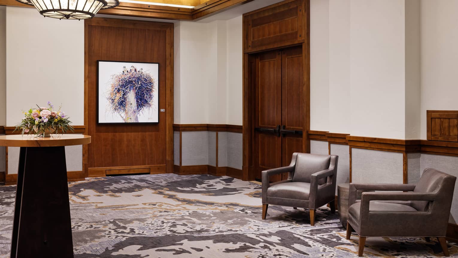 The corner of a room with two chairs, art on the wall and a standing table.