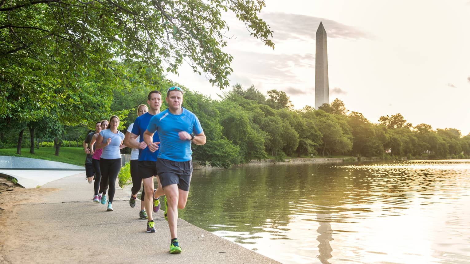 Row of men, women running on path beside water 