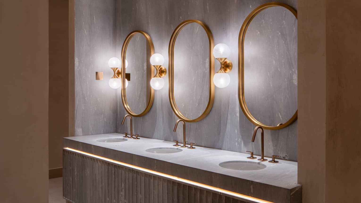Three-sink concrete vanity with three oval mirrors above each sink and three double-globe light fixtures