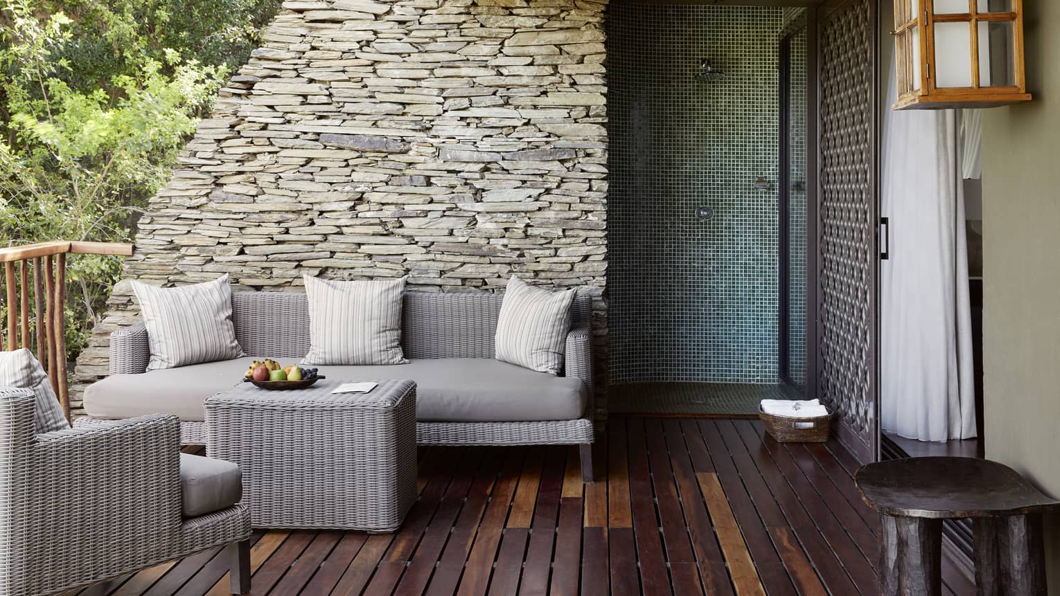 Wood-slatted terrace with neutral wicker seating vignette against stacked stone wall and sliding door to right