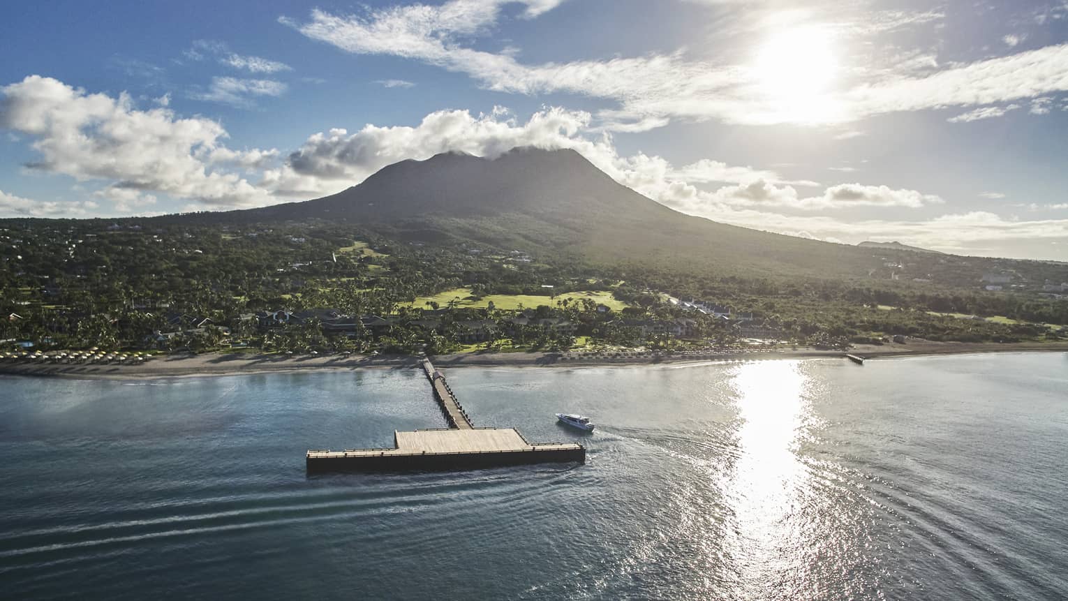 Aerial view of sun shining over Nevis mountain, lagoon with large wood bridge and dock