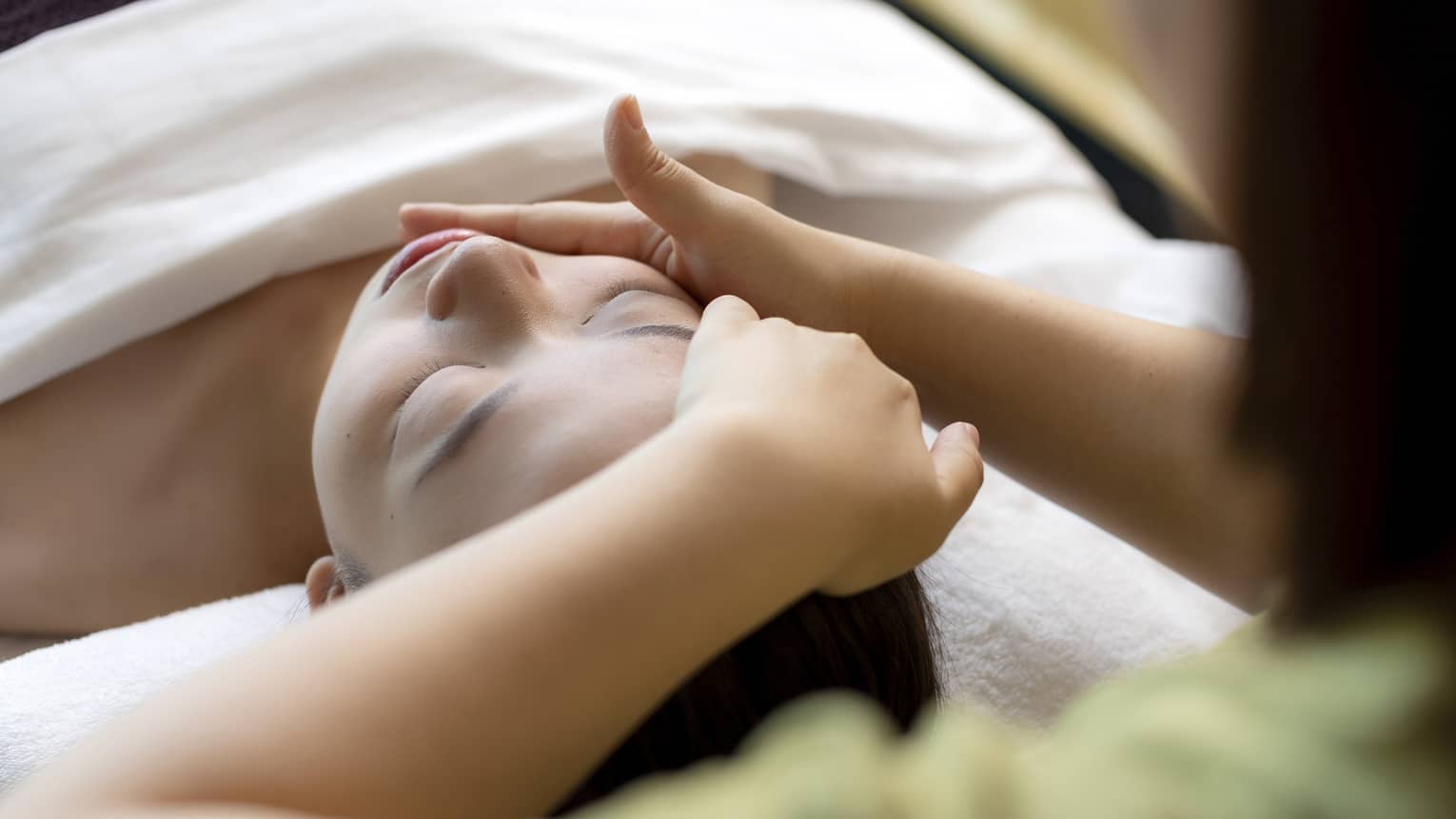 Hua Spa staff massages woman's face as she lays on treatment table