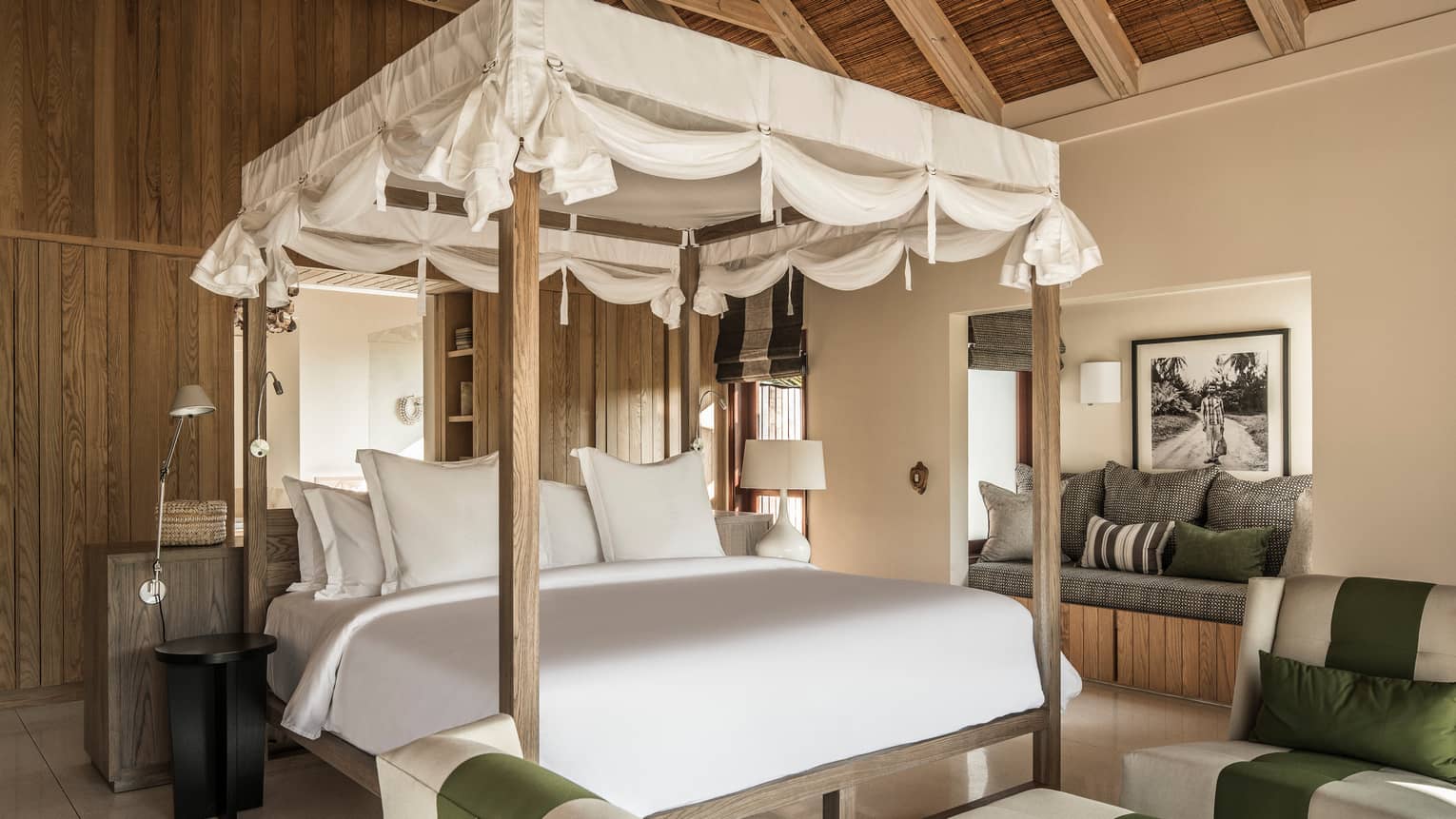White canopy with ties at top of poster bed, behind sofas and cushioned bench