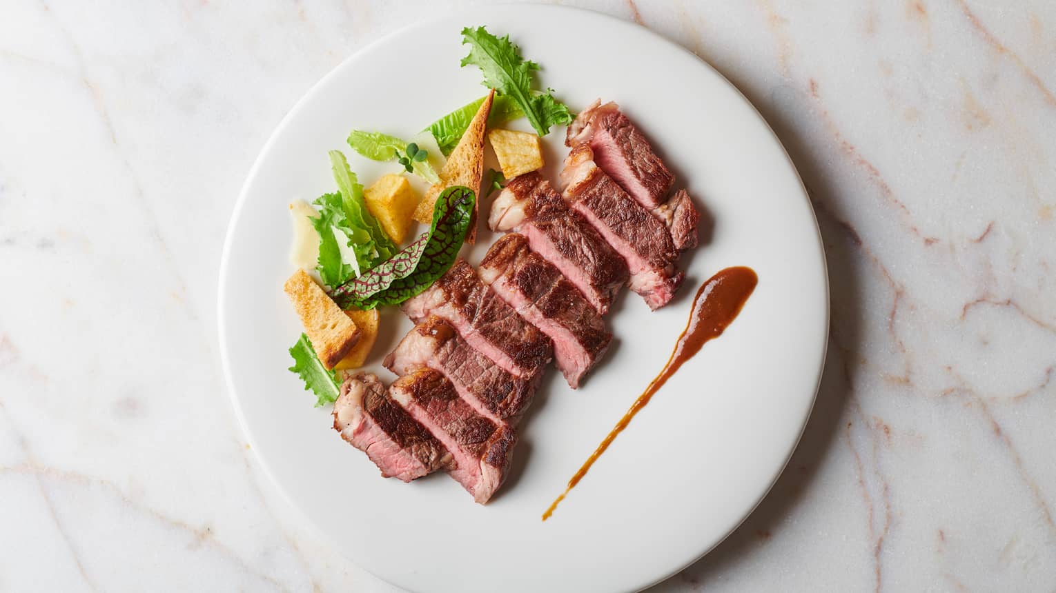 Strips of seared beef on plate with salad, sauce garnish