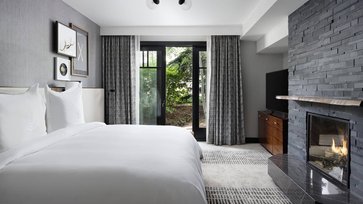 Guest room with King bed, stone fireplace, glass doors leading to terrace, chest of drawers with TV
