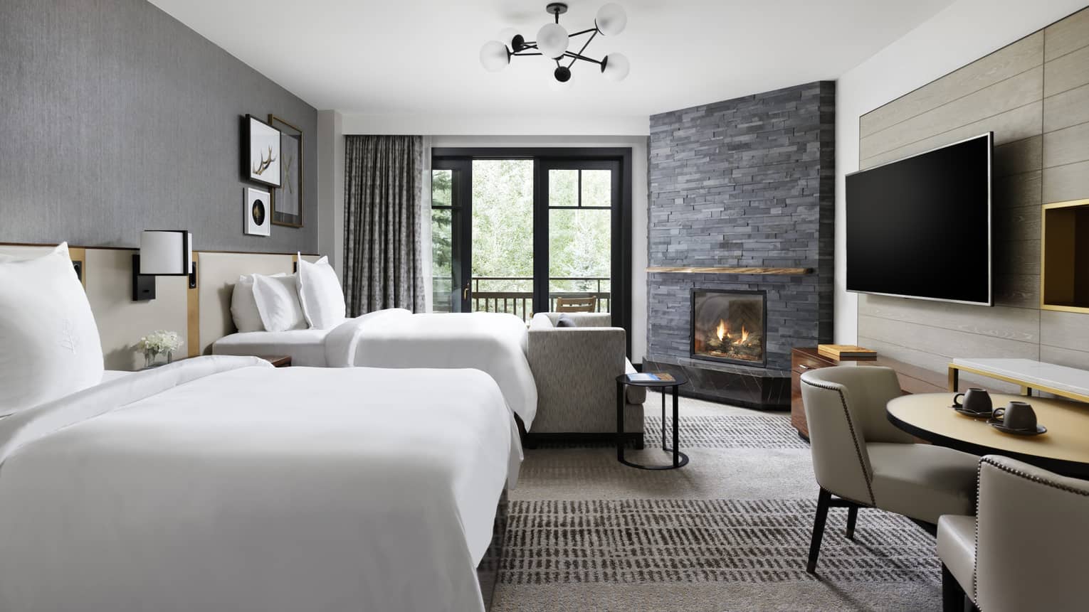 Guest room with two double beds, small table and two chairs, corner fireplace, sliding glass doors leading to balcony