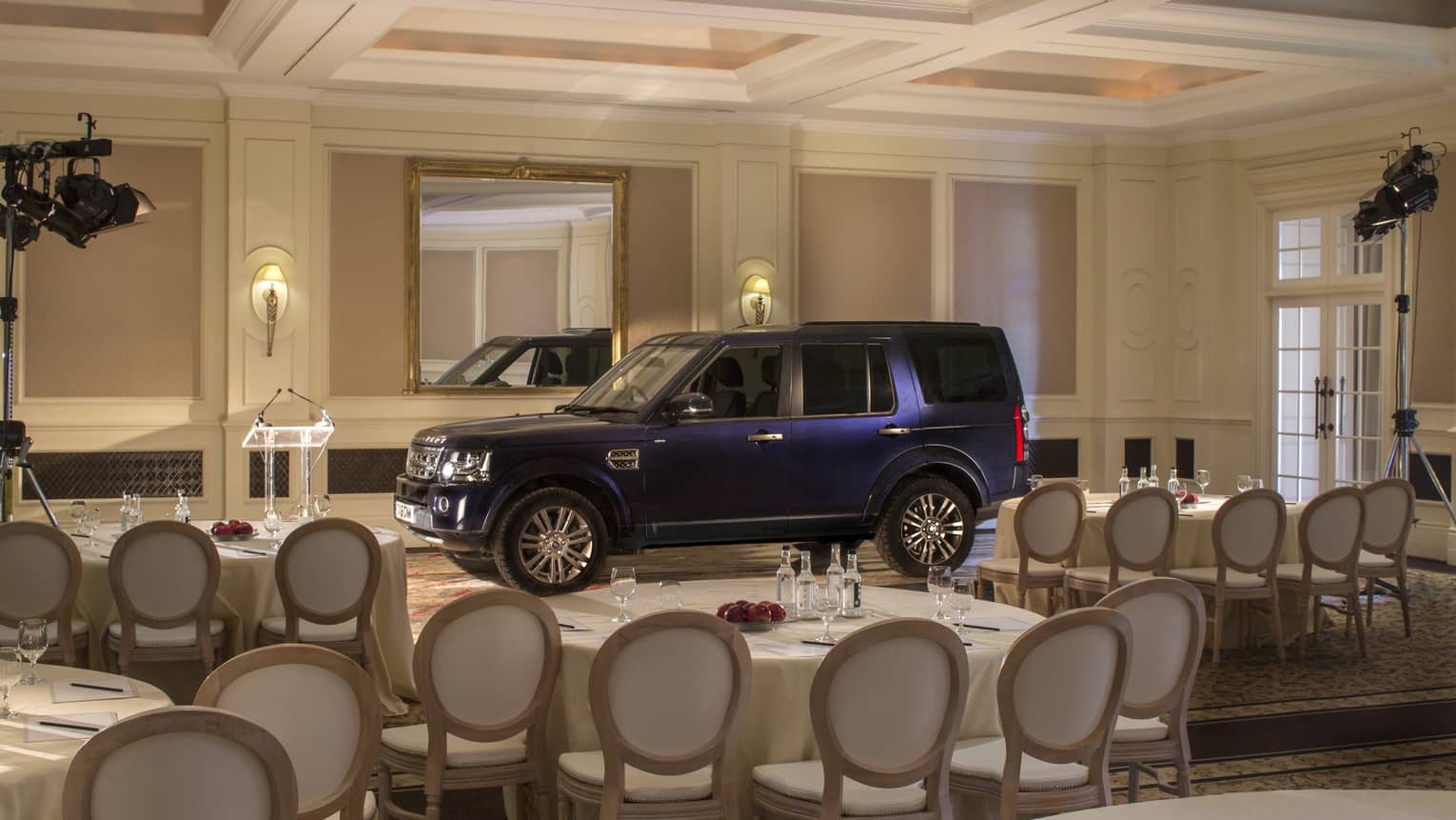 S U V car parked inside ballroom, surrounded by banquet tables and chairs